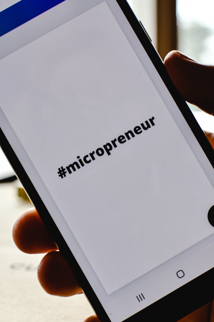 Close-up of a hand holding a smartphone with the hashtag #micropreneur on screen, symbolizing entrepreneurship.